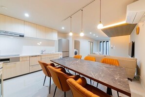 A modern kitchen with a marble countertop, wooden cabinets, and a dining area with orange chairs. - SUMISORa Osaka (Osaka)