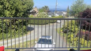 A balcony with wicker furniture, a view of a road, and houses in the background. - Cross the Street to the Beach & Ocean Views (Victoria)