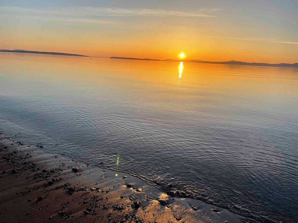 Un coucher de soleil sur une étendue d’eau calme, avec une rive.
