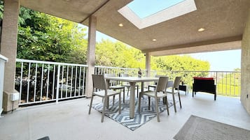 Une terrasse extérieure couverte, équipée d’une table et de chaises, d’un barbecue et offrant une vue sur les arbres.