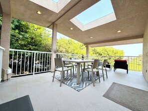 Eine überdachte Terrasse im Freien mit Tisch, Stühlen und einem Grill, mit Blick auf Bäume.