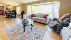 A living room with a sofa, a coffee table, and a rug. There is a window providing natural light. - Cross the Street to the Beach & Ocean Views (Victoria)
