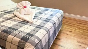 A bedroom with a checkered bedspread, a bedside table, a window with a view of trees, and a wooden floor. - Cross the Street to the Beach & Ocean Views (Victoria)