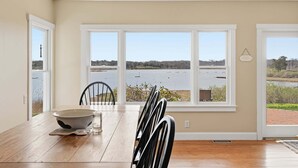 A dining area with a view of a lake, a white table, chairs, and a bowl. - Waterfront Chatham Escape, Pet Friendly, Pond Views & Beach Nearby (Chatham)