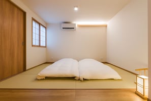 Een kamer met tatami vloer, een schuifdeur, een raam met shoji schermen en een luchtverwarmer aan het plafond.