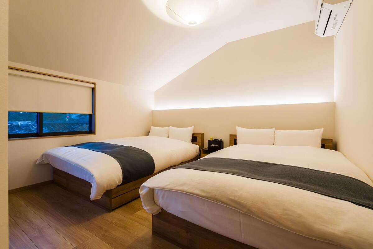 Ein Schlafzimmer mit zwei Betten, einem Fenster mit Blick, einer Deckenleuchte und einer Klimaanlage.