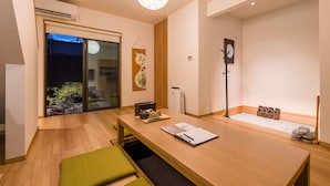 Un interior moderno con una mesa de comedor de madera, un banco verde, un reloj de pared y una puerta de vidrio corredera que da a un jardín.