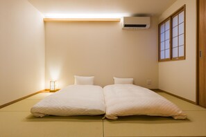 A room with tatami flooring, a bed with white bedding, an air conditioner, a window with shoji screens, and a bedside table with a lamp. - Miro Gion Yasaka Tei (Kyoto)
