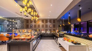 A modern buffet setup with a central island, multiple food stations, and a seating area with orange chairs. - Crystal Hotel Shanghai Intl. Tourism (Shanghai)