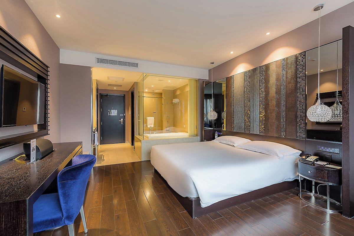 A hotel room with a bed, desk, chair, and a large mirror.