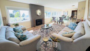 A spacious living room with a fireplace, two sofas, a coffee table, and a large window. - 3BR Edgemont Retreat | Views, Deck, Near Grouse (North Vancouver)