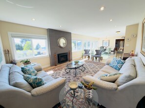 A spacious living room with a fireplace, two sofas, a coffee table, and a large window. - 3BR Edgemont Retreat | Views, Deck, Near Grouse (North Vancouver)