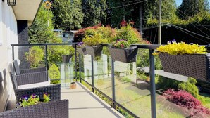 A balcony with wicker furniture, a glass railing, and potted plants. - 3BR Edgemont Retreat | Views, Deck, Near Grouse (North Vancouver)