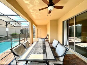 Eine sonnendurchflutete Terrasse mit Pool, einem Tisch und Stühlen sowie einem Deckenventilator.