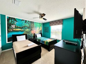 Ein Zimmer mit zwei Betten, einem Schreibtisch, einem Deckenventilator und einem großen Wandgemälde.