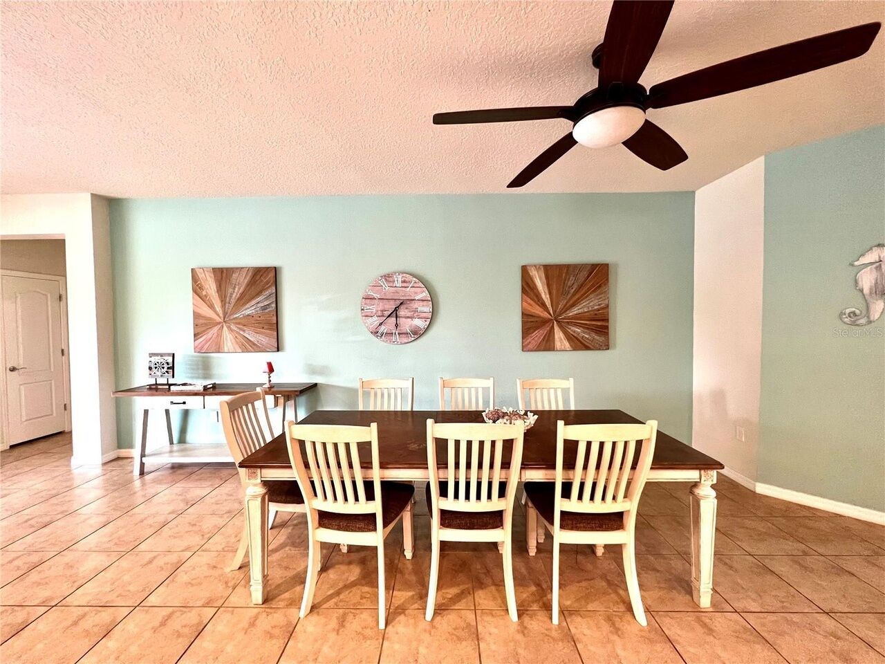 Een eethoek met een tafel en stoelen, een plafondventilator en kunstwerken aan de muur.