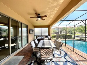 Eine überdachte Terrasse mit Pool, Gartenmöbeln und Deckenventilator.