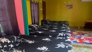 Varias camas con ropa de cama floral, un ventilador de techo y piso de baldosas.
