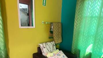 A room with a bed, a window with curtains, a door with a mirror, and a wall with a door handle.