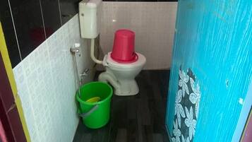 A small bathroom with a toilet, a green bucket, and a white toilet paper holder.