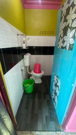 A small bathroom with a toilet, a green bucket, and a white toilet paper holder. - Hotel O Green Desa Bayu (Sungai Petani)