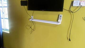 A room with a yellow wall, a flat-screen TV mounted on it, a power outlet, and a granite countertop.