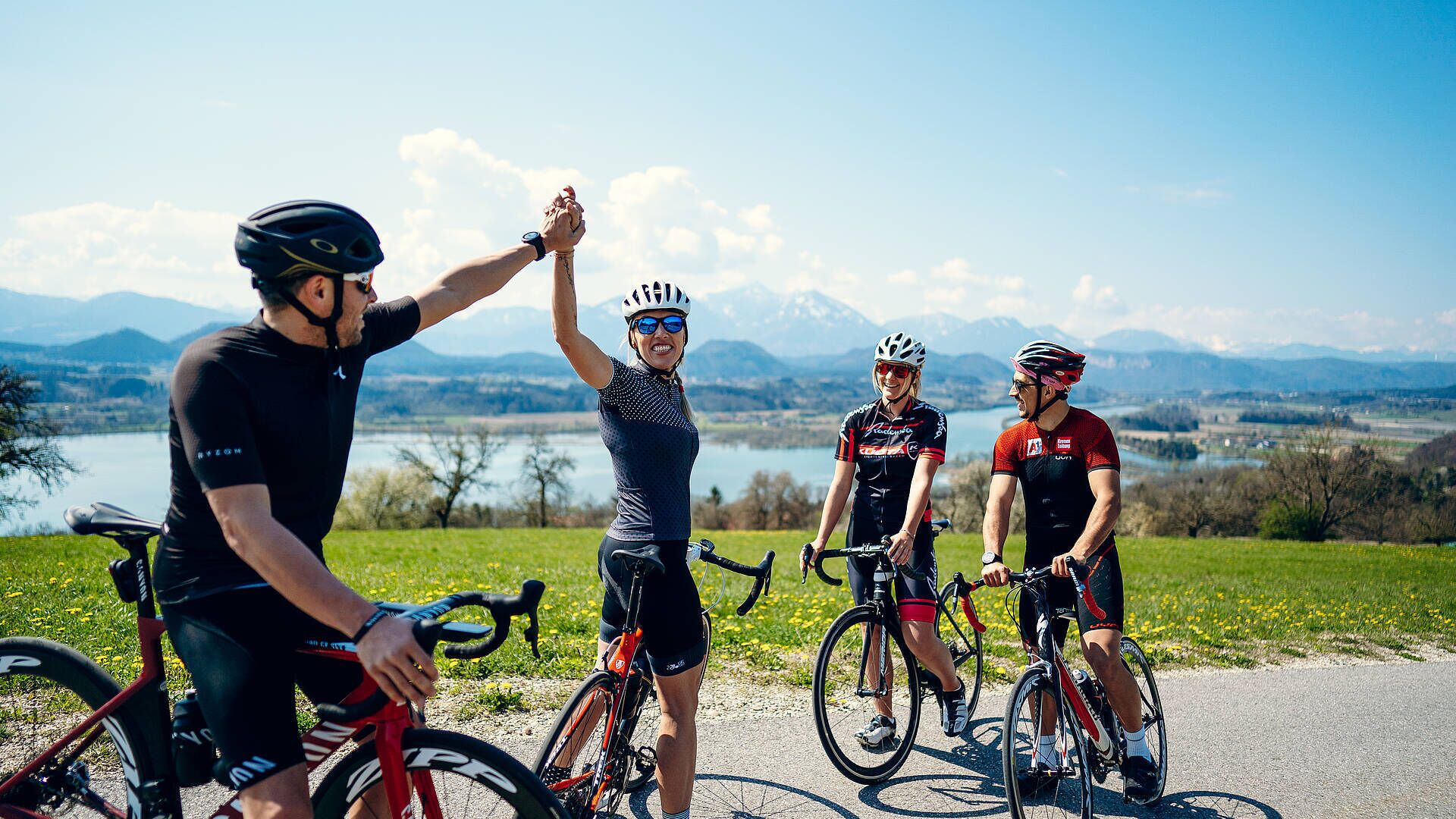 A group of cyclists on a road with a scenic view of mountains and a lake.