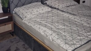 A bedroom with a large bed, a headboard, a wall-mounted TV, and two potted plants. - Quiet vacation apartment near Lake Klopeinersee (Völkermarkt)