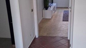 A hallway with red-tiled flooring leading to a room with a window, a plant, and a bench. - Quiet vacation apartment near Lake Klopeinersee (Völkermarkt)