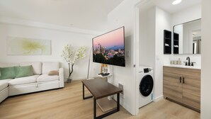 Een moderne woonkamer met een bank, een salontafel, een televisie en een wasmachine op de achtergrond.