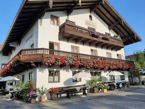 A traditional Alpine-style building with a balcony adorned with flowers, outdoor seating, and a sign indicating it is a guesthouse.