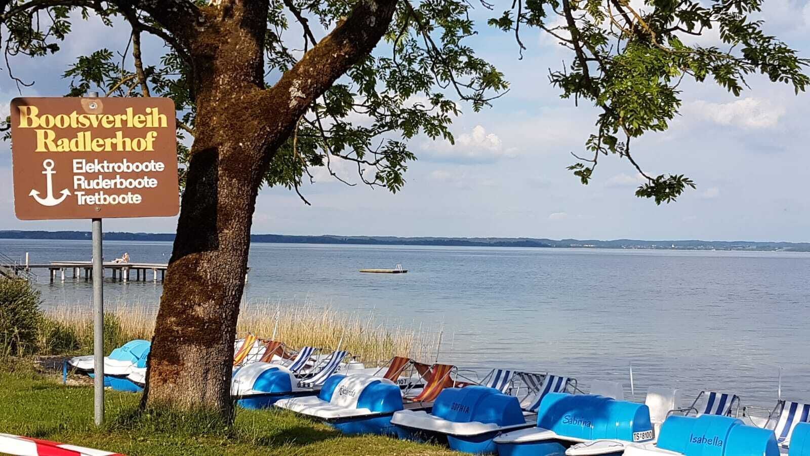 A lakeside view with a sign for Bootsverleih Radlerhof, indicating rental services for boats.