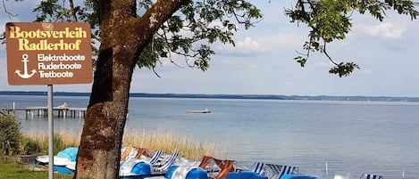 Vista al lago con un cartel de Bootsverleih Radlerhof, indicando servicios de alquiler de embarcaciones.
