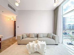 Ein modernes Wohnzimmer mit einer Eckcouch, einem einzigartigen weißen Couchtisch und einem großen Fenster mit Blick auf die Stadt.