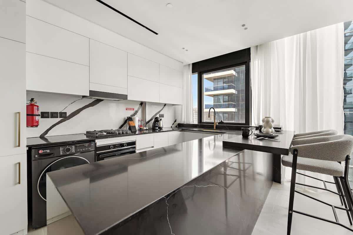 Una cocina moderna con una isla central, armarios blancos y un amplio ventanal.