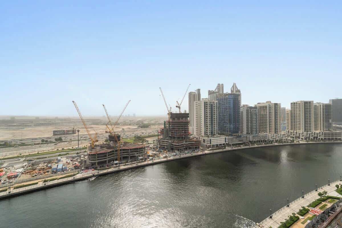 Stadsgezicht aan het water met hoge gebouwen, kranen en een rivier.