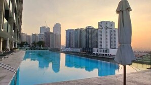 Una piscina con sillas de descanso y sombrillas, rodeada de edificios altos.