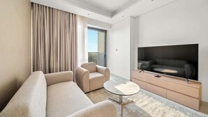 A modern hotel room with a sofa, armchair, TV, and a glass door leading to a balcony. - Modern 1BR in Brand-New Cloud Tower in JVT (Dubai)