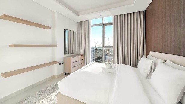A modern hotel room with a large bed, a dresser, and a view of the cityscape. - Modern 1BR in Brand-New Cloud Tower in JVT (Dubai)