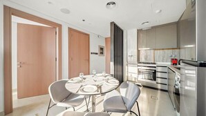 A modern kitchen with stainless steel appliances, a dining area with a round table and chairs, and a large window providing natural light. - Modern 1BR in Brand-New Cloud Tower in JVT (Dubai)