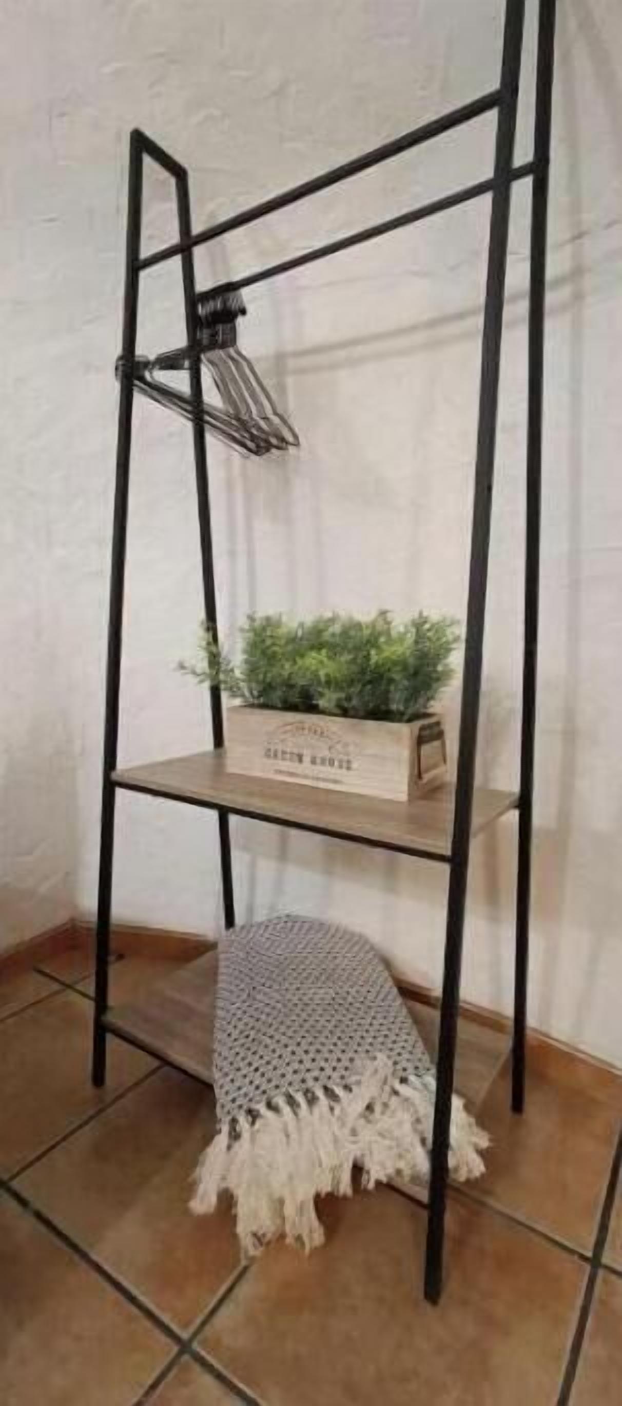 A black metal shelf unit with a woven mat at the bottom and a wooden box with greenery on the middle shelf.