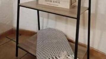 A black metal shelf unit with a woven mat at the bottom and a wooden box with greenery on the middle shelf.