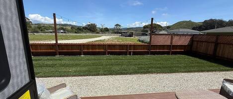 Une terrasse dotée de meubles en osier et offrant une vue sur un espace clos, avec de l’herbe et des bâtiments situés au loin.
