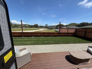 Terras met rieten meubilair en uitzicht op een omheind gazon met gebouwen in de verte.