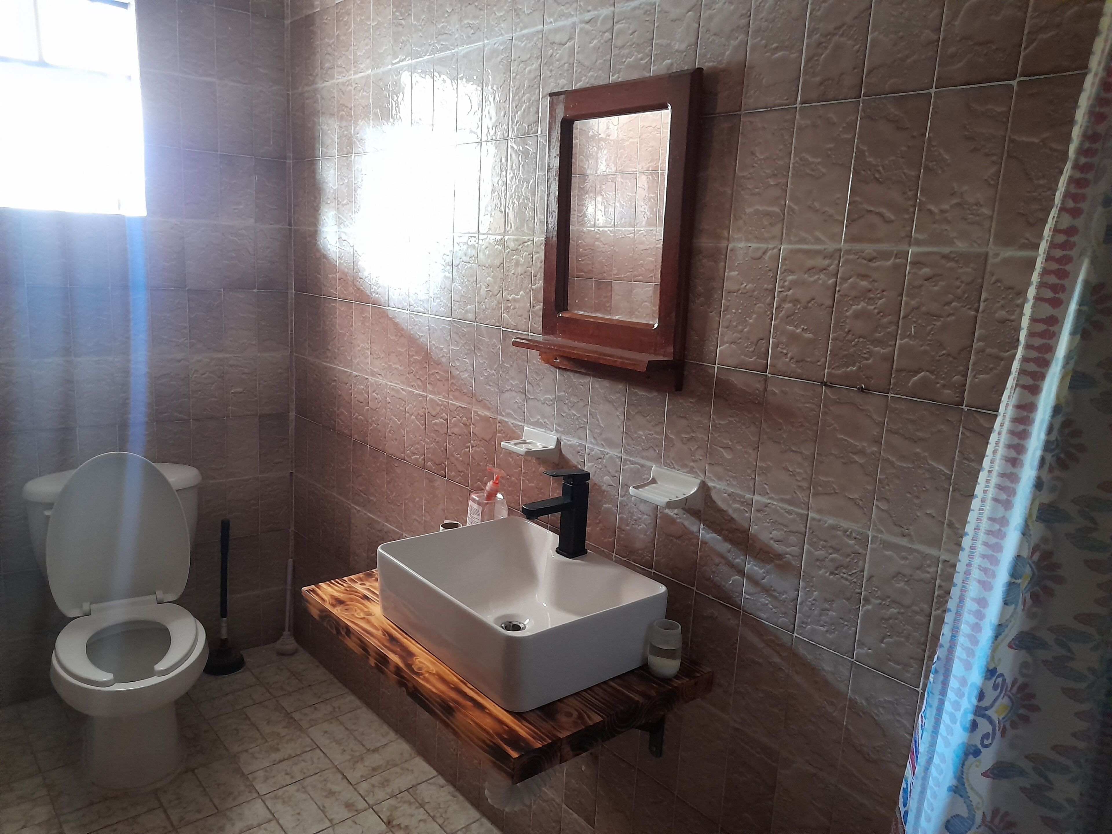 Uma casa de banho com sanita, lavatório com espelho e cortina de chuveiro.