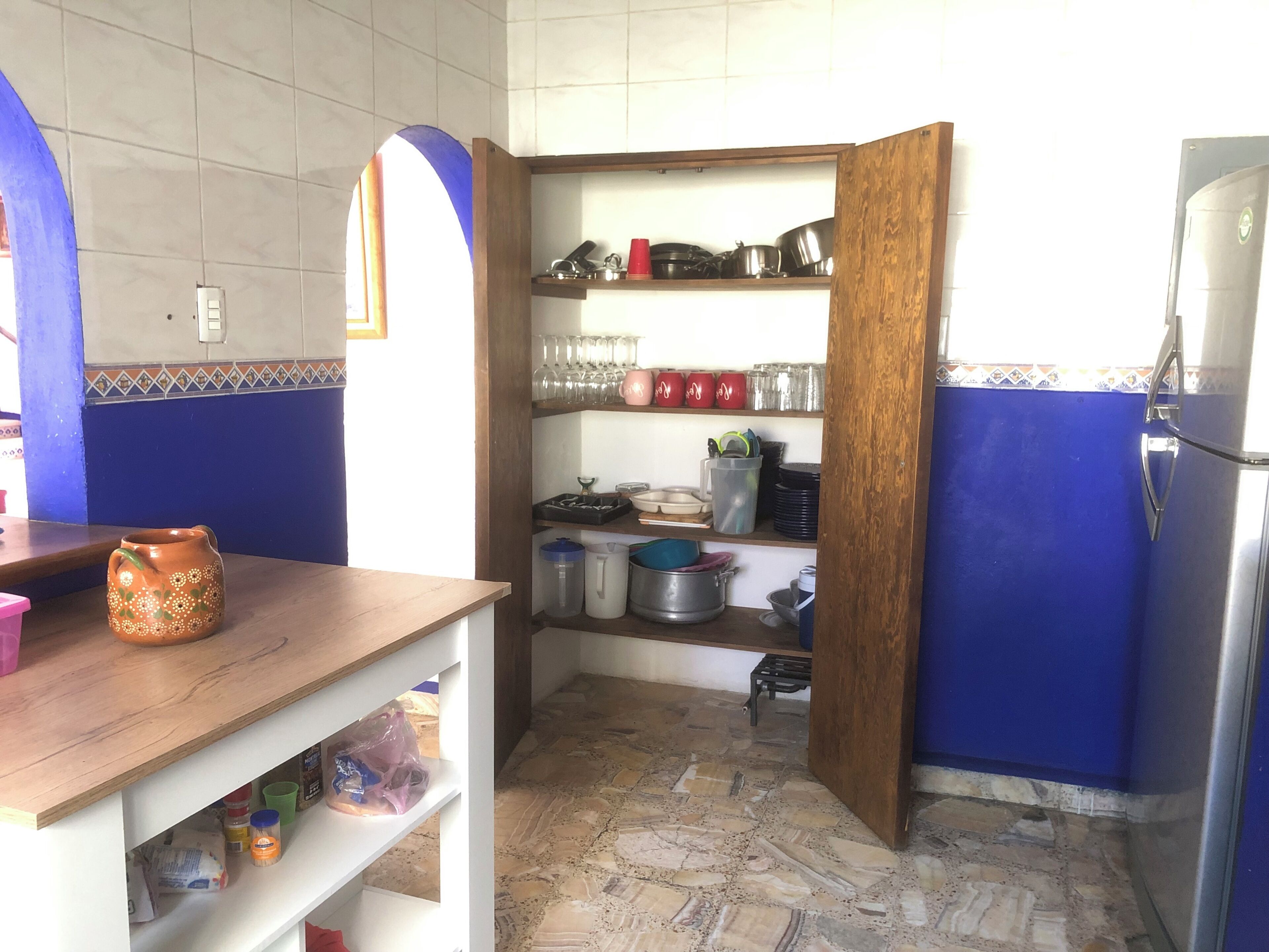A kitchen with a blue wall, a wooden counter, and shelves with kitchenware.