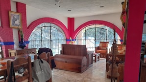 A room with a wooden sofa, a dining table with chairs, a large arched window, and a decorative wall. - Casa Quinta Don Ricardo (Francisco Villa)