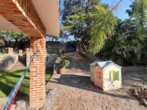Un edificio in mattoni con un piccolo giardino, una casetta per bambini e una scala in pietra che conduce a un cancello.