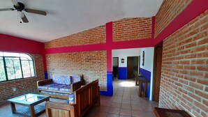 A room with a brick wall, a wooden sofa, a wooden table, and a ceiling fan. - Casa Quinta Don Ricardo (Francisco Villa)