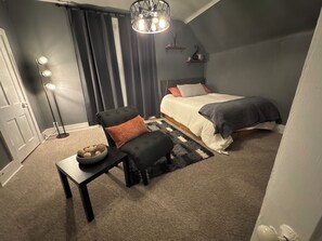A bedroom with a bed, a chair, a table, and a floor lamp.